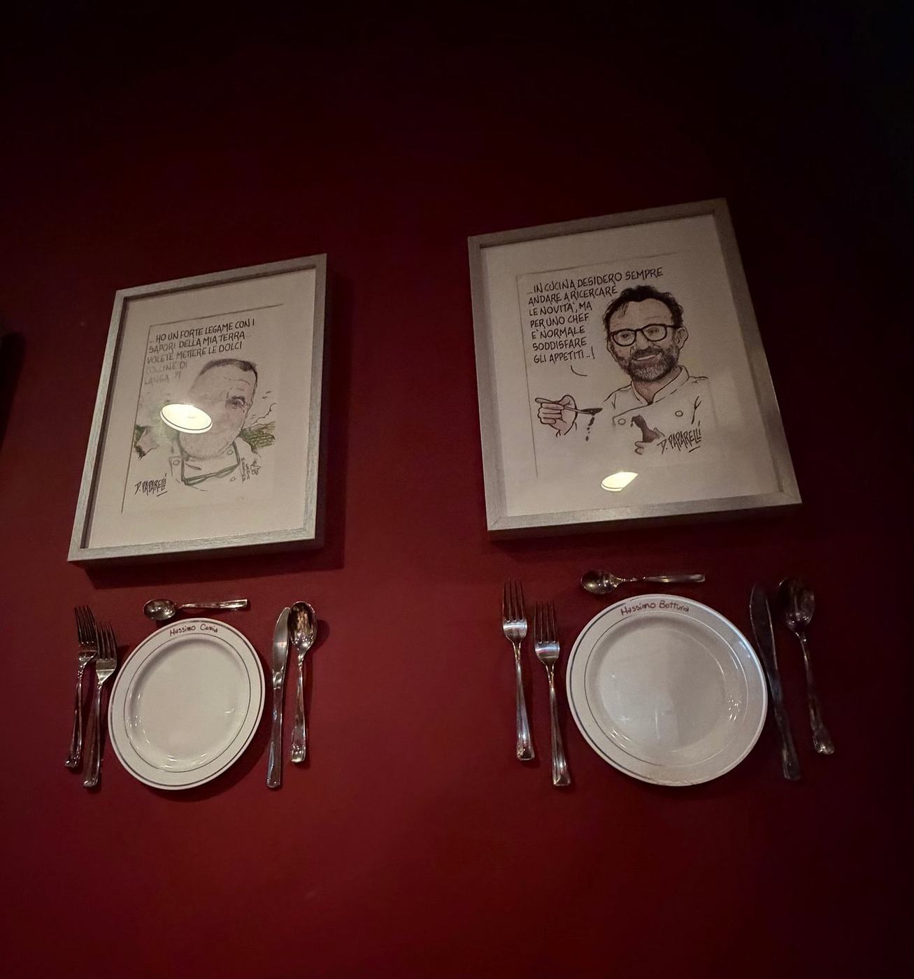 Due caricature di chef incorniciate su una parete bordeaux, ciascuna con piatto e posate appesi sotto