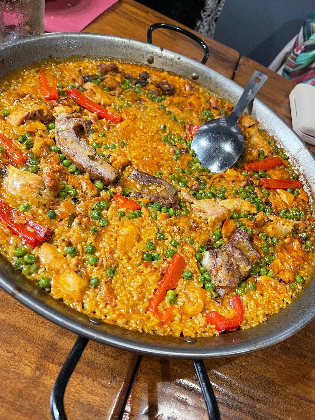 Paella valenciana con carne, piselli e peperoni rossi nella paellera