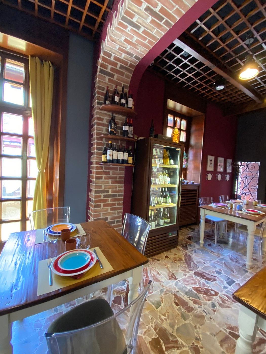 Saletta con arco in mattoni a vista, pareti bordeaux, vetrina dei vini e tavoli apparecchiati