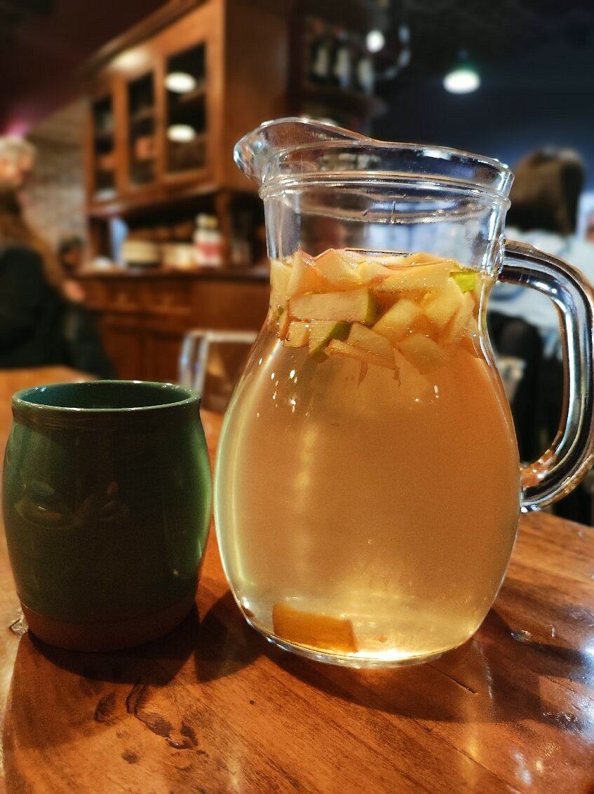 Caraffa di sangria bianca con pezzi di mela accanto a un bicchiere di ceramica verde